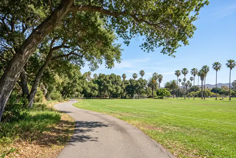 Shaded park path with old oak trees and a sports field in an Encino-style neighborhood