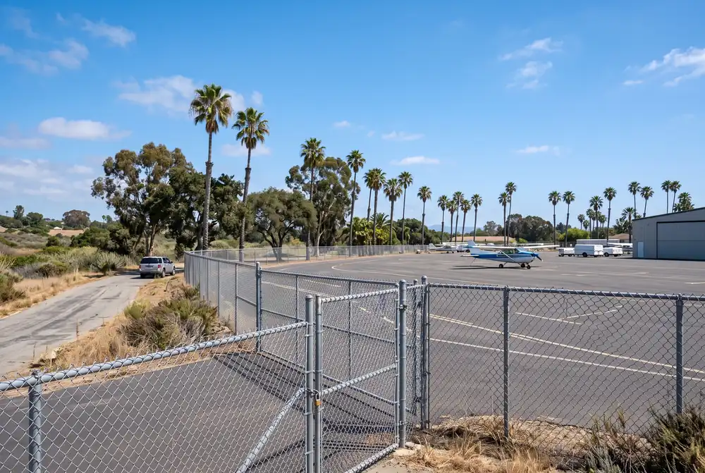 Small airport runway fence with palm trees under a clear sky in a Van Nuys-style setting
